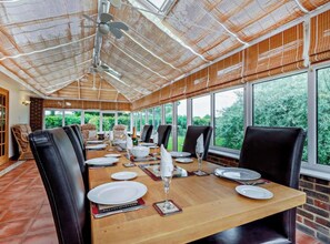 Ein Essbereich mit einem langen Holztisch, gedeckt für eine Mahlzeit, große Fenster mit Blick auf Grünflächen und eine Decke mit einem einzigartigen Webdesign.