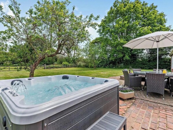 Ein Whirlpool in einem Hinterhof mit einer Terrassenfläche, Gartenmöbeln und einem großen Sonnenschirm.