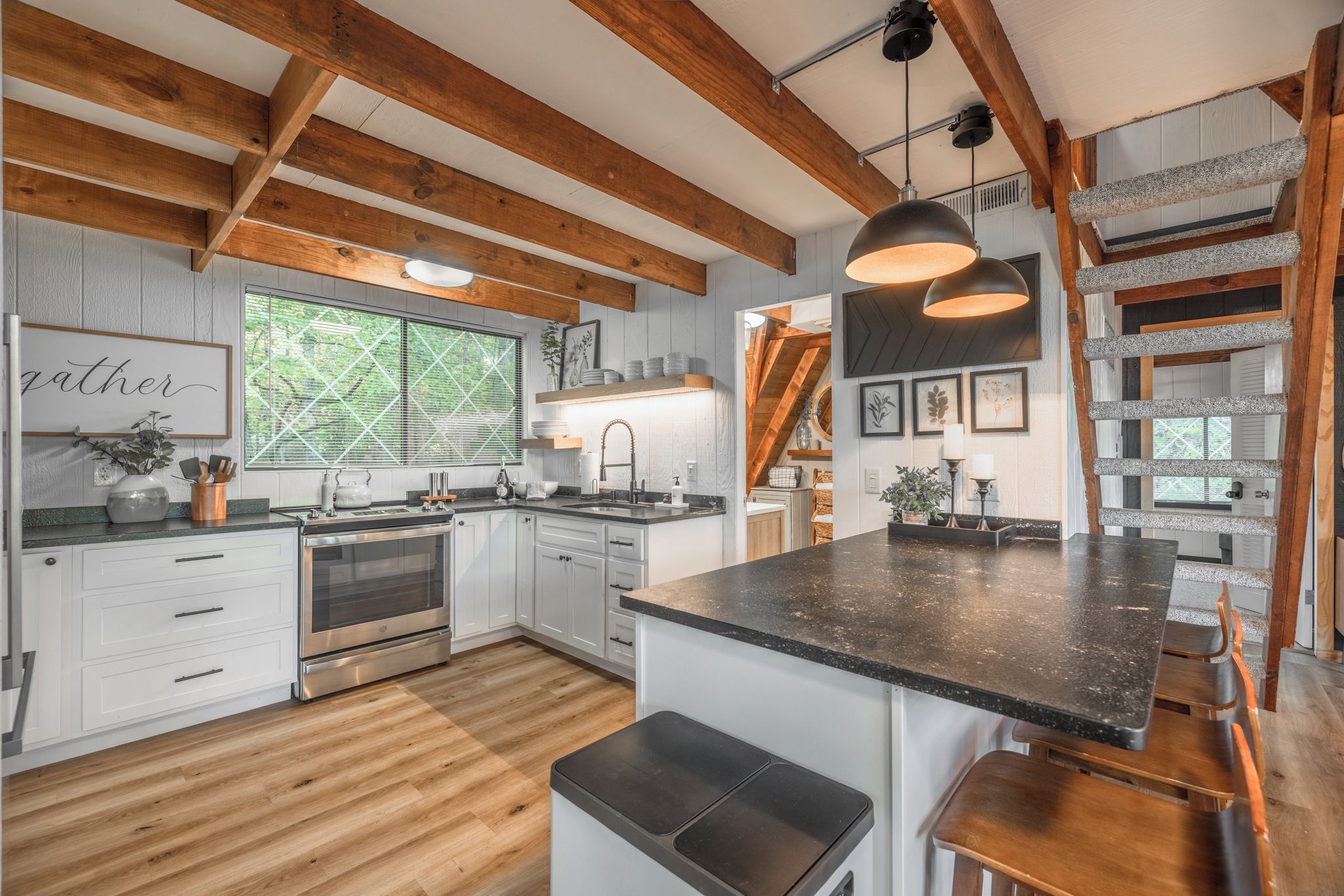 A modern kitchen with wooden beams, a large island, and a view of the outdoors.