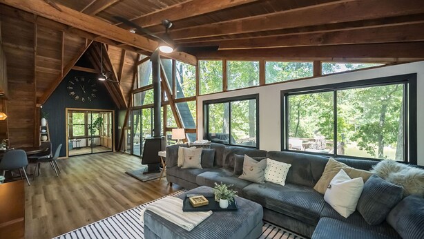 A spacious living room with a large couch, a coffee table, and a fireplace. There are large windows providing natural light and a view of the outdoors. - Foxfire Shores Escape by Innsbrook Vacations! (Innsbrook)