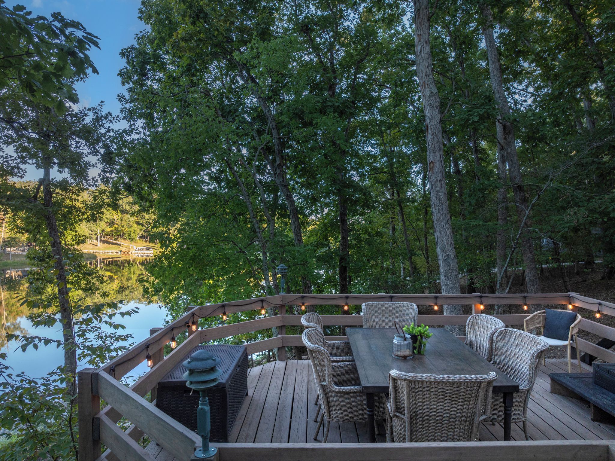 A wooden deck with wicker furniture and string lights, overlooking a body of water.