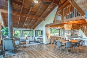 A spacious living area with a high ceiling, wooden beams, a fireplace, and a dining area with modern chairs. - Foxfire Shores Escape by Innsbrook Vacations! (Innsbrook)