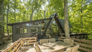 A wooden deck with wicker furniture and a glass-enclosed structure with a chimney. - Foxfire Shores Escape by Innsbrook Vacations! (Innsbrook)