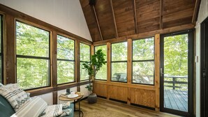 A cozy room with a wooden ceiling, large windows, a blue sofa, a small table with a plant, and a view of the outdoors. - Foxfire Shores Escape by Innsbrook Vacations! (Innsbrook)
