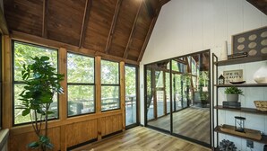 A cozy room with wooden walls and large windows, a round table with a plant, and a bookshelf with various items. - Foxfire Shores Escape by Innsbrook Vacations! (Innsbrook)