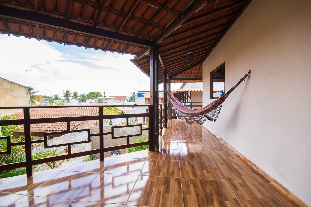 A wooden balcony with a hammock, a tiled floor, and a view of the neighborhood.