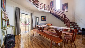 A spacious dining area with a wooden table and benches, a staircase with a railing, and artwork on the walls. - Casa com 3 Su tes Climatizadas na Ilha da Croa (Barra de Santo Antonio)