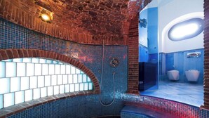 Um banheiro moderno com uma janela em arco singular, paredes com azulejos azuis e área de chuveiro aparente.