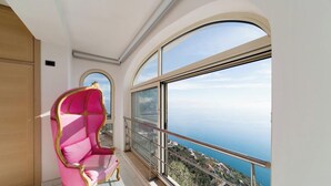 Uma varanda com uma cadeira rosa e uma janela ampla com vista para a costa.