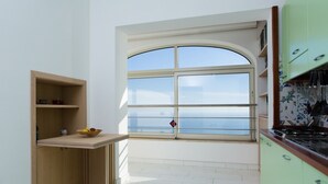 Uma cozinha com uma janela grande, bancada de madeira e vista para o mar.