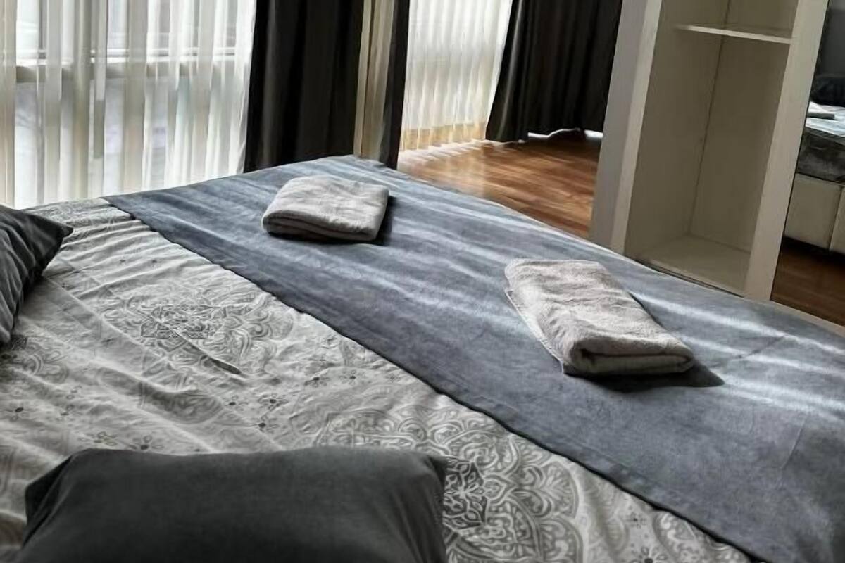 A bedroom with a large bed, a wardrobe, and a view through sheer curtains.