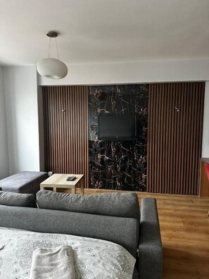 A modern bedroom with a bed, a TV mounted on a marble wall, a wooden panel wall, and a small wooden table. - D&D PANSİYON (Istanbul)