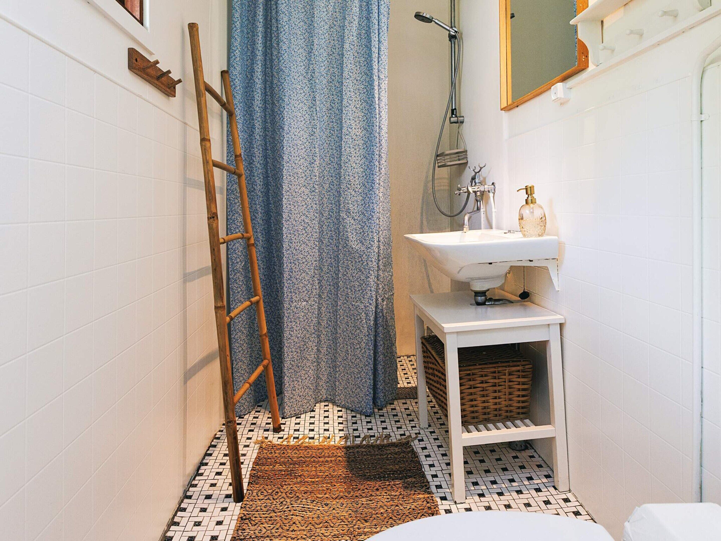 A bathroom with a white sink, a shower, a wooden ladder, a patterned shower curtain, and a tiled floor.
