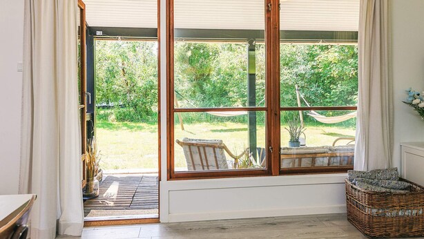 A room with a large sliding glass door leading to a garden, a wicker basket, and a small table with a chair. - 5 Person Holiday Home in Rodby (Rodby)