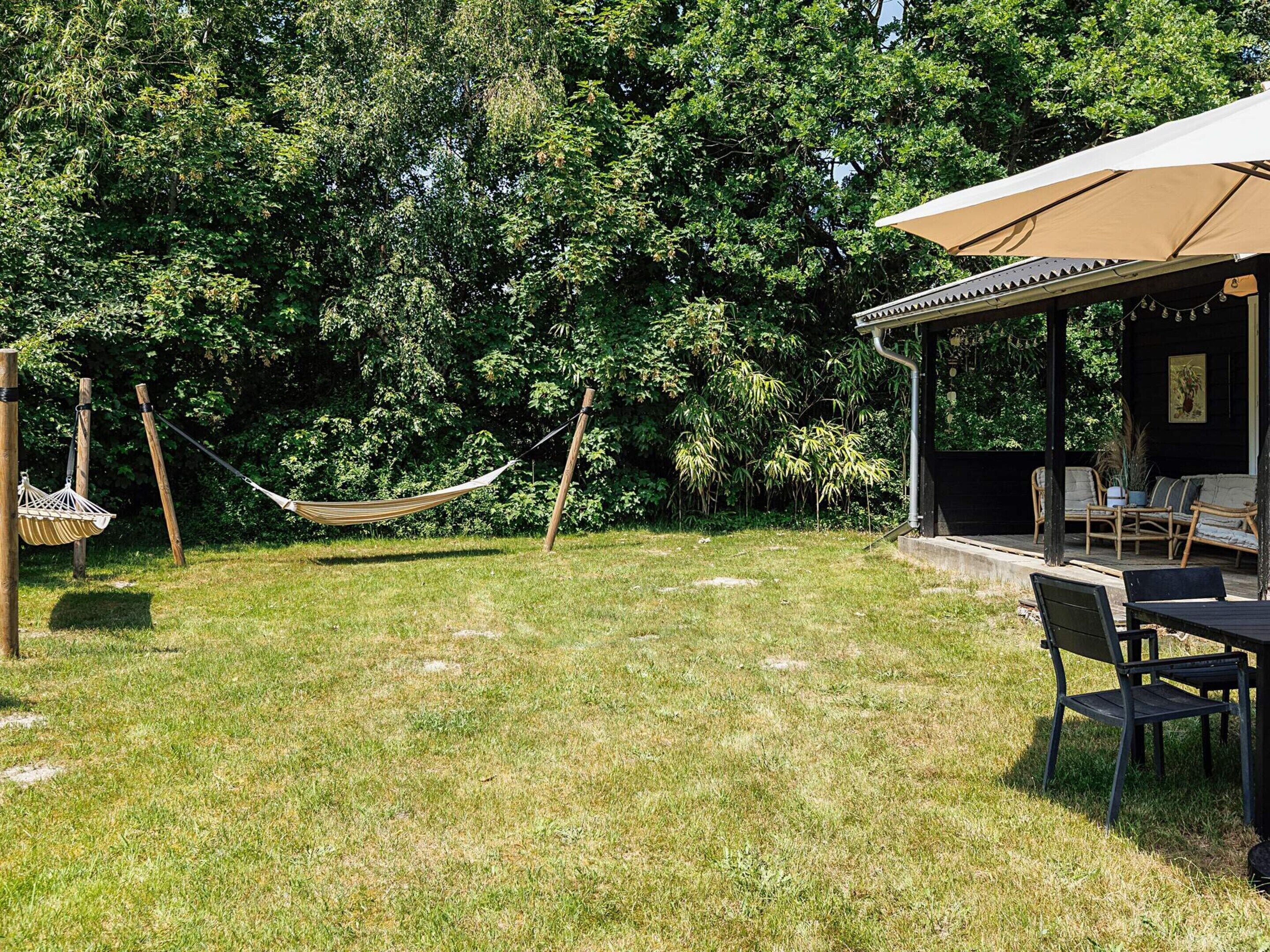A grassy backyard with a hammock, a covered seating area with chairs, and a dining table.