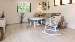 A living room with a sofa, a rocking chair, a small table, a window with a view of greenery, and a wall-mounted air conditioner. - 5 Person Holiday Home in Rodby (Rodby)