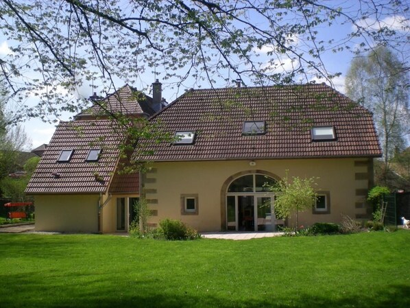 A two-story house with a tiled roof, a front entrance with glass doors, and a small garden area.