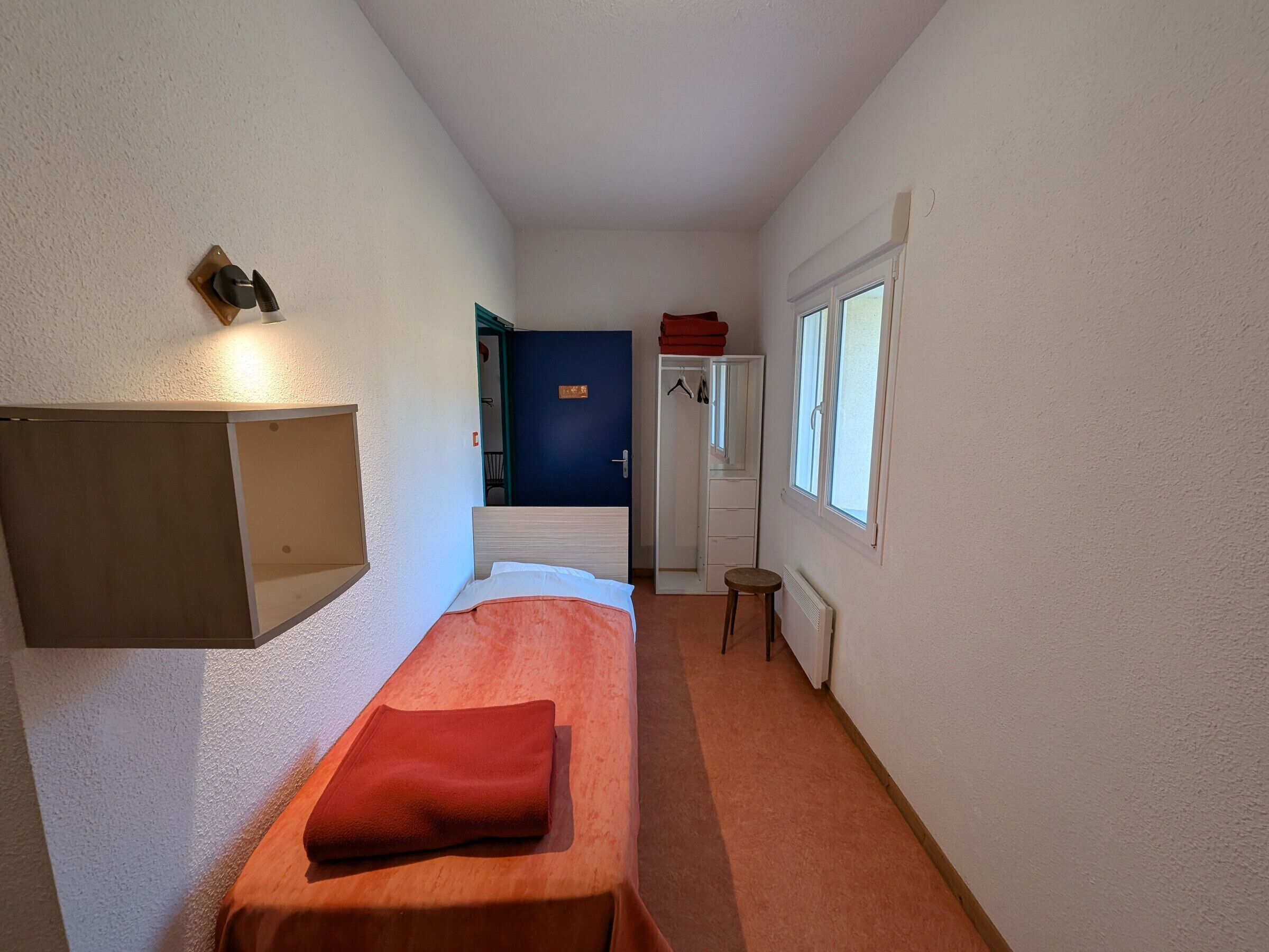 A narrow hallway with a bed on the left, a wardrobe on the right, and a door at the end.