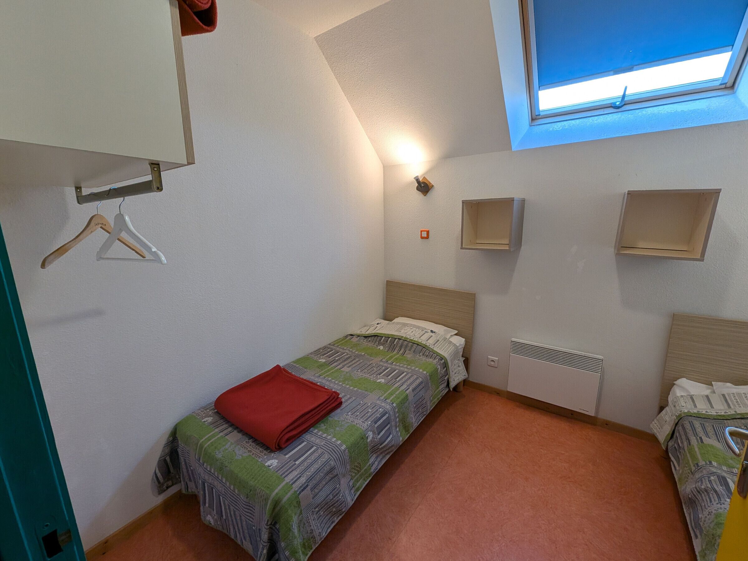 Un dormitorio pequeño y bien iluminado con una cama individual, un radiador y una ventana con vistas.