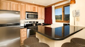 Une cuisine moderne avec des meubles en bois, des appareils électroménagers en acier inoxydable, un grand îlot central avec des tabourets et une vue sur un paysage montagneux par la fenêtre.