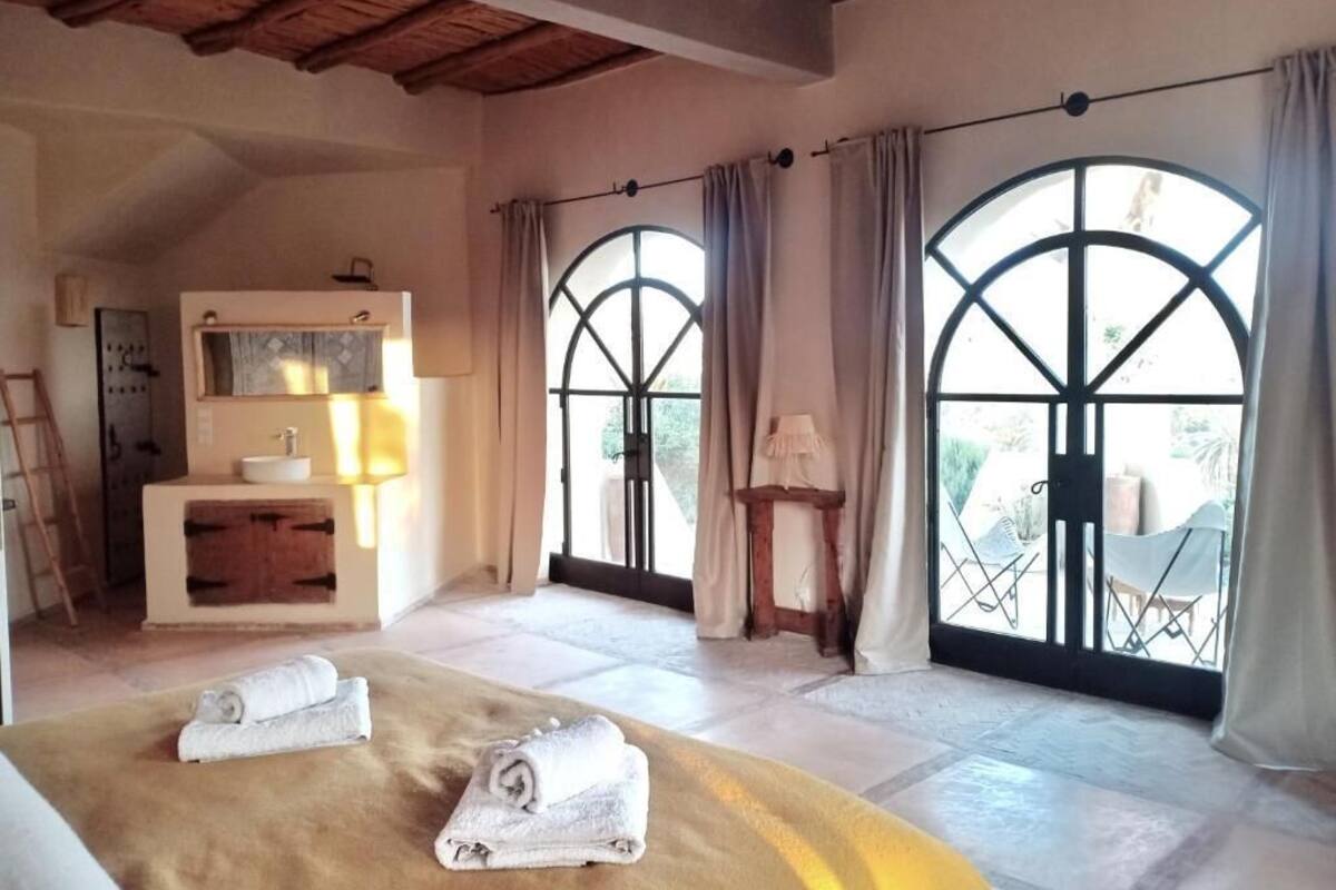A bedroom with a bed, a vanity with a mirror, and large arched windows.