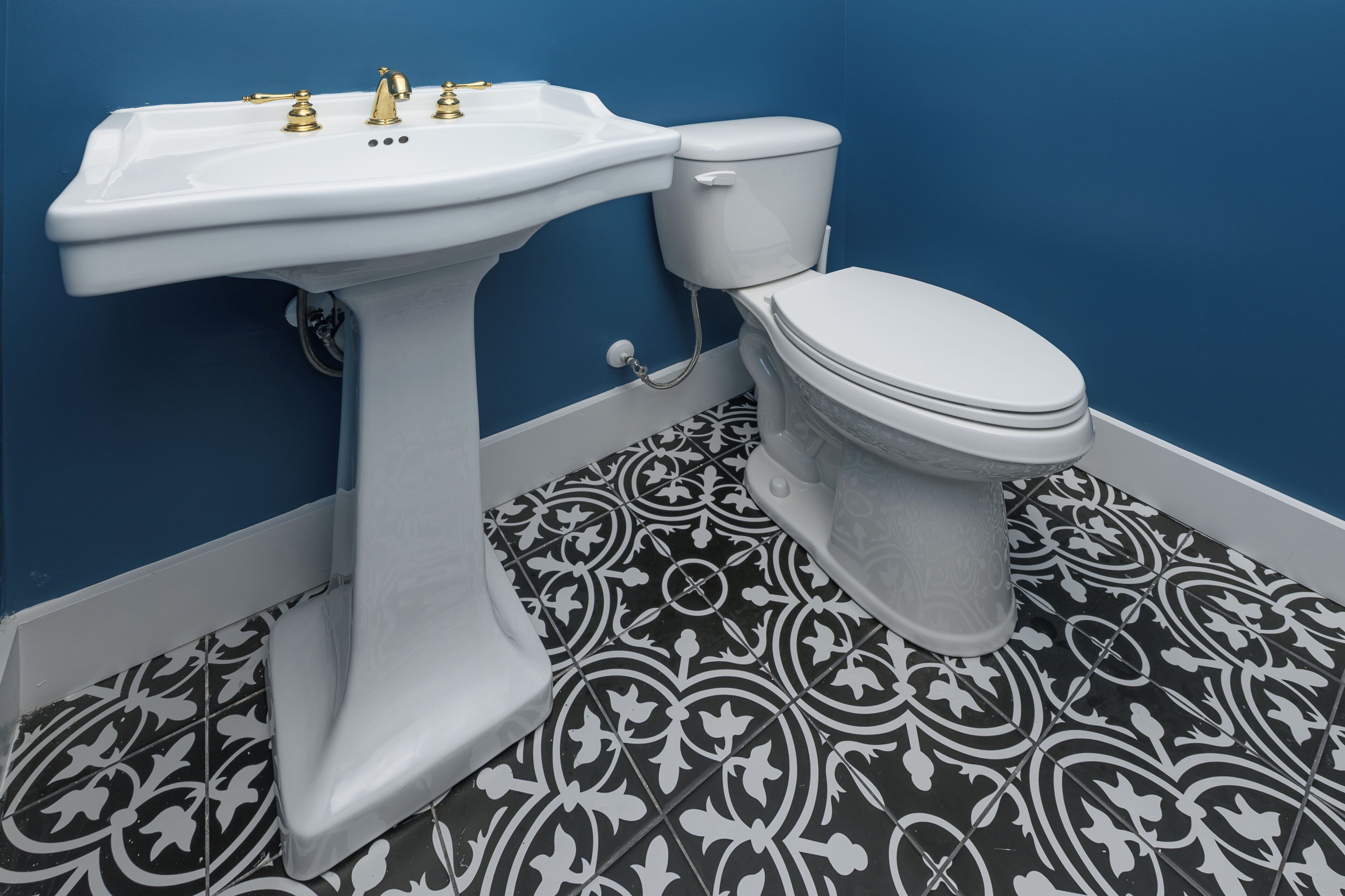 A bathroom with a pedestal sink, toilet, and patterned floor tiles.