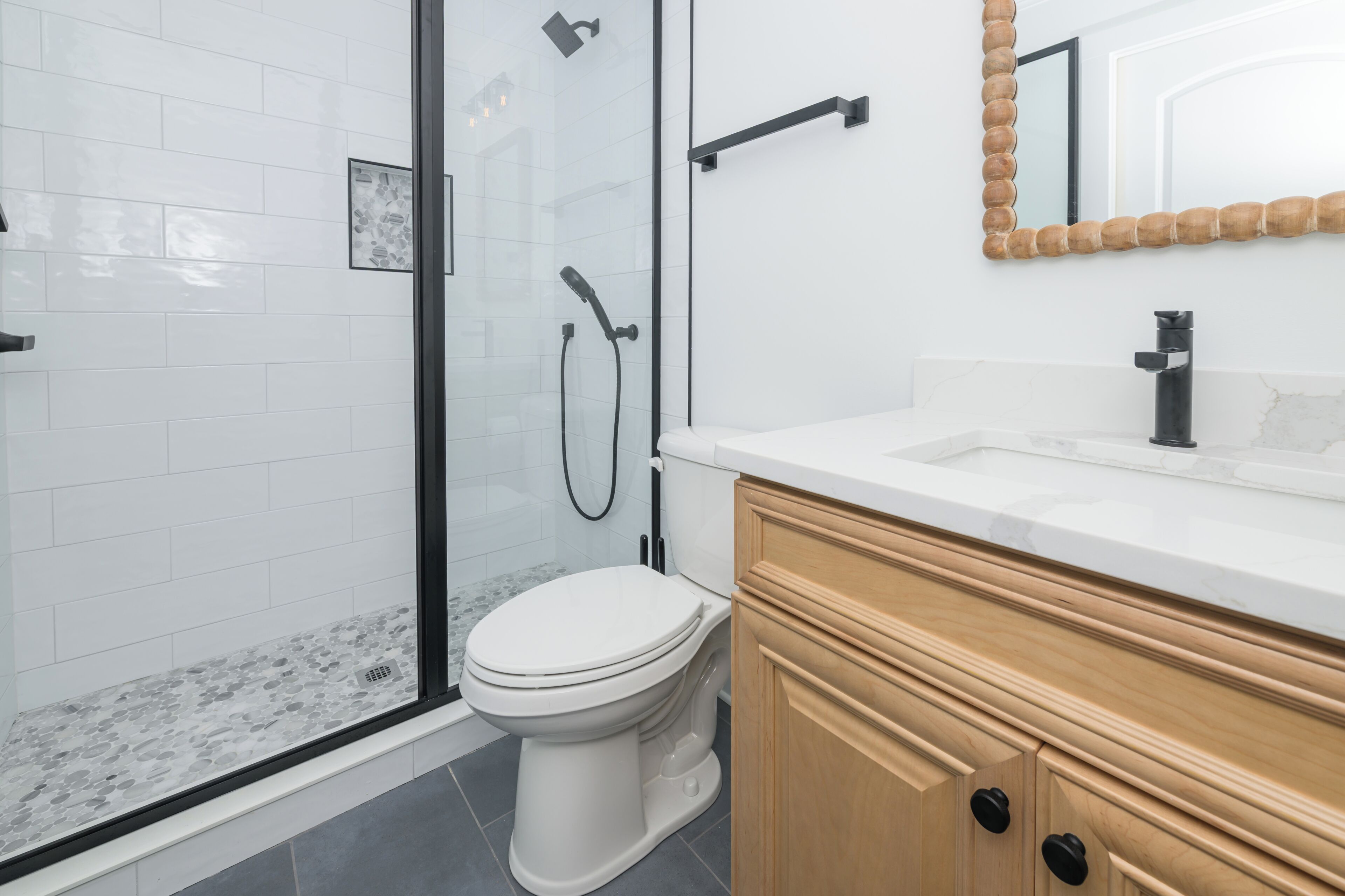 Et moderne badeværelse med glasvæg omkring brusebad, toilet i hvidt og træskabe.