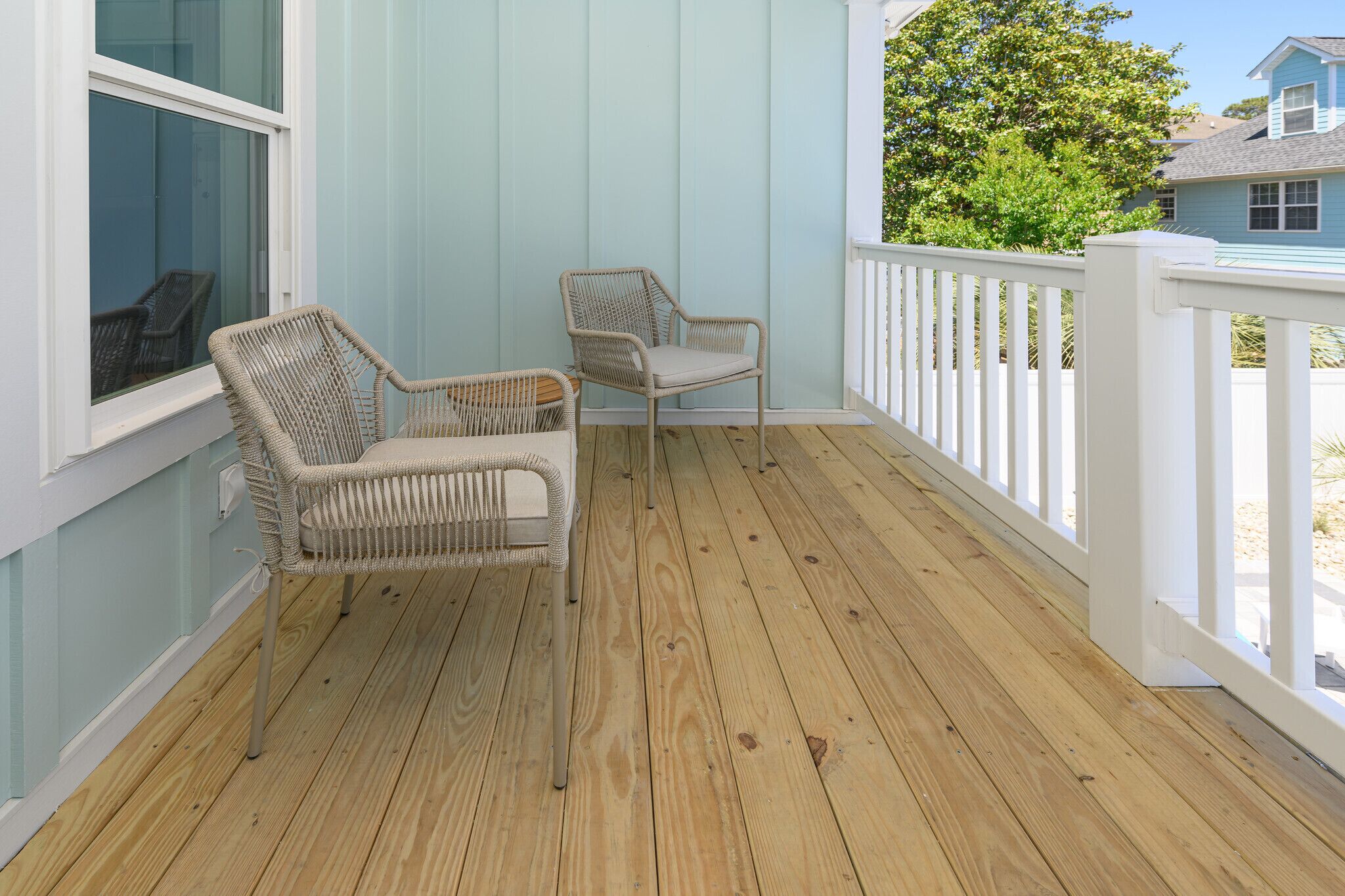 A wooden deck with two wicker chairs and a white railing.