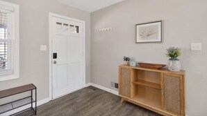Un corridoio con una porta bianca, un tavolino consolle in legno con oggetti decorativi e un quadro appeso al muro.