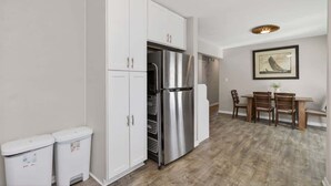 Una cucina compatta con mobili bianchi, un frigorifero in acciaio inossidabile e un'area pranzo con sedie e tavolo in legno.