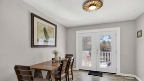 Un'area pranzo con un tavolo e sedie in legno, un quadro appeso al muro e una porta scorrevole in vetro che dà su un patio esterno.