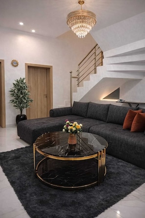 A modern living room with a black marble coffee table, grey sofa, and a staircase with a railing. - Cozy 2 Bedroom Terrace Duplex + Wi-Fi,TV,24/7 Power In Ajah (Lekki/Ajah)