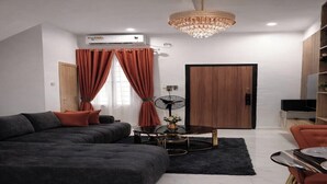 A modern living room with a sectional sofa, a round coffee table, and a chandelier. - Cozy 2 Bedroom Terrace Duplex + Wi-Fi,TV,24/7 Power In Ajah (Lekki/Ajah)