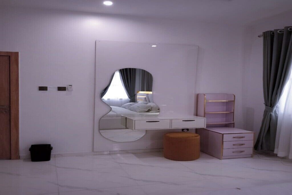 A bedroom with a large mirror, a bedside table, a wardrobe, and a small stool.