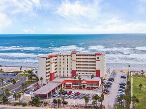 Un hotel con fachada roja y blanca, un estacionamiento y vistas al océano.