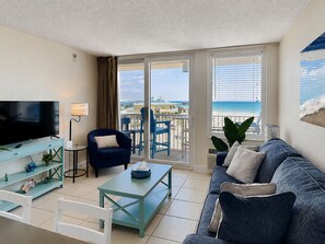 Ein Wohnzimmer mit Fernseher, einer Couch, einem Couchtisch und einem Balkon mit Blick auf den Strand.