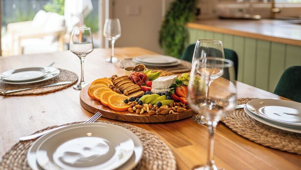 Una tavola imbandita con piatti, posate e un tagliere di frutta e formaggi.