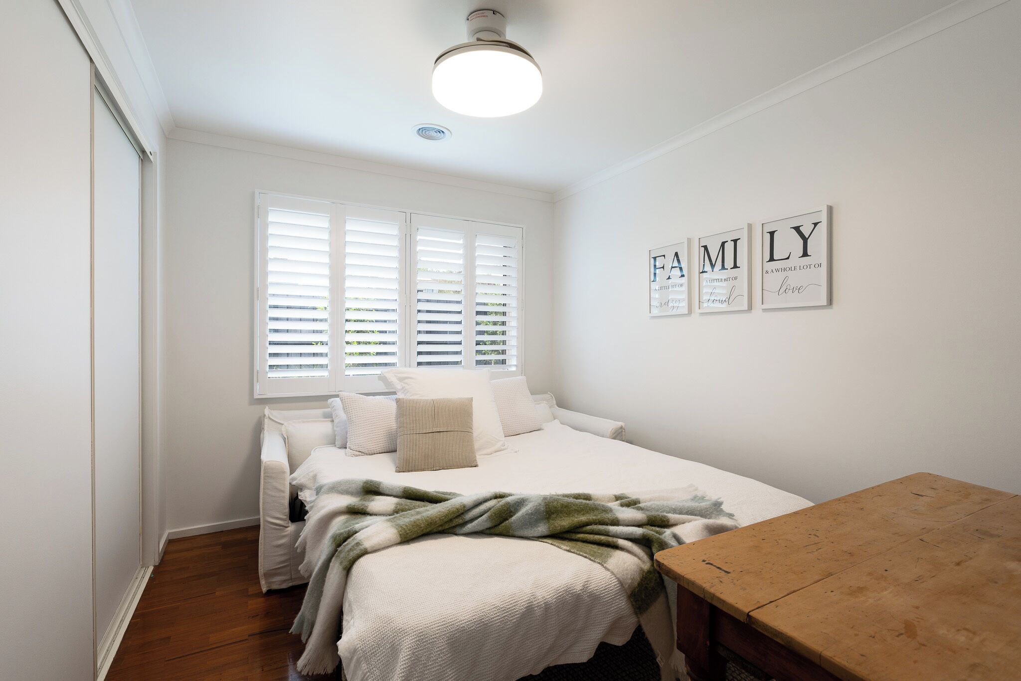 Quarto com cama, mesa de madeira e janela com persianas.