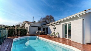 A modern house with a swimming pool, wooden deck, and a patio area with outdoor furniture. - Villa with private pool, garden & wood stove (Le Teich)