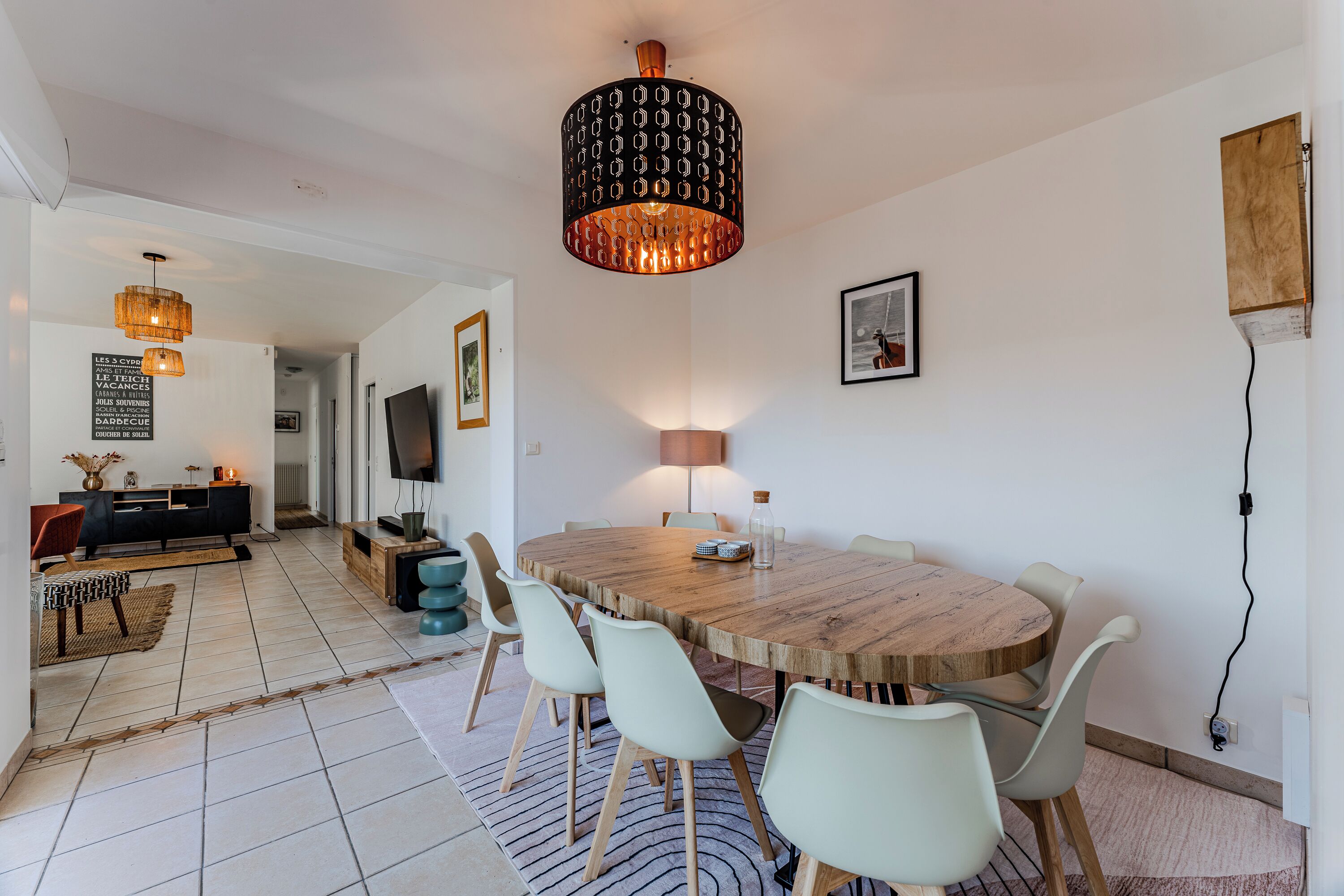 A modern dining area with a round wooden table, white chairs, and a unique patterned pendant light.