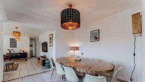 A modern dining area with a round wooden table, white chairs, and a unique patterned pendant light. - Villa with private pool, garden & wood stove (Le Teich)