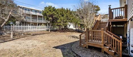 Wooden deck and stairs lead to a spacious backyard surrounded by coastal trees and neighboring properties.