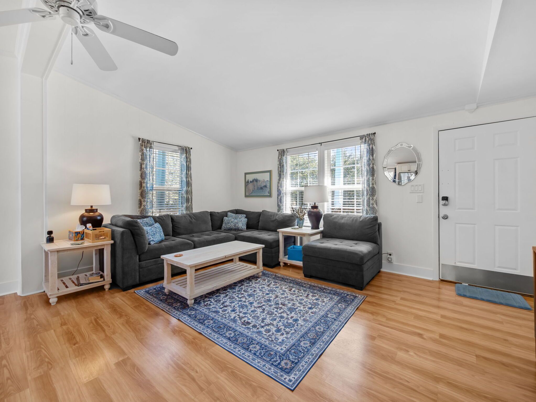Unwind on the plush sectional sofa in your bright, airy living room featuring gleaming hardwood floors and charming coastal decor.