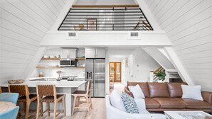 A modern loft apartment with a kitchen, dining area, and living room. - A-Frame of Mind - Stylish Santa Rosa Beach Retreat | Walk to Beach (Santa Rosa Beach)