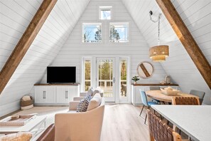 Una habitación estilo loft con techo inclinado, televisor integrado, comedor y ventanas amplias.