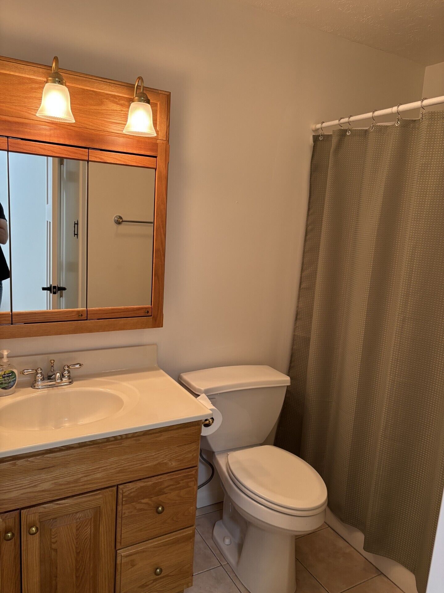 Un baño con tocador de madera, lavamanos blanco, inodoro y cortina de ducha.