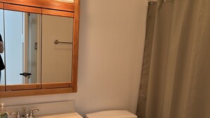Een badkamer met een houten wastafelmeubel, een witte wastafel, een toilet en een douchegordijn.