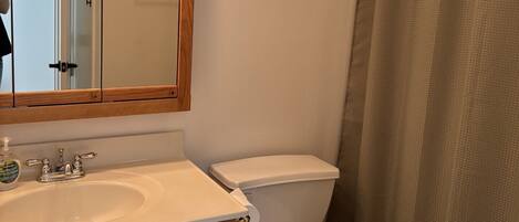 Un baño con tocador de madera, lavamanos blanco, inodoro y cortina de ducha.