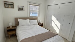 Een slaapkamer met een bed, nachtkastje, raam en deur.