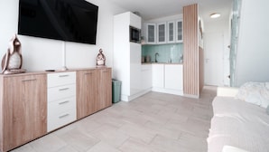 A modern, well-lit room with a large flat-screen TV mounted on the wall, a wooden cabinet with drawers, a small trash bin, and a bed with a patterned blanket. - Light Filled Property Near Sea (Agde)